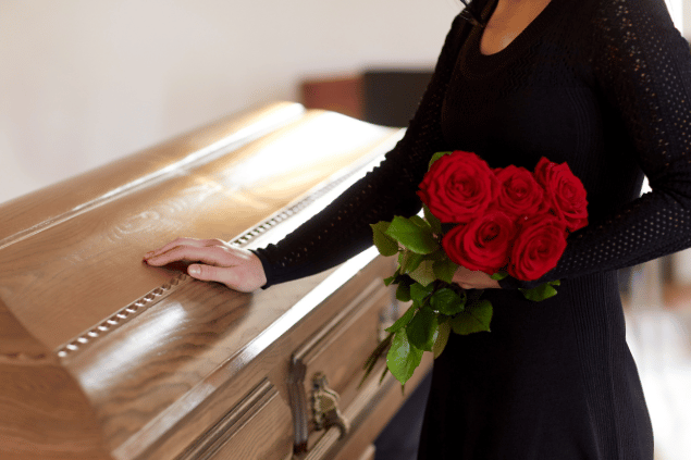 Mulher segurando rosas, com mão sobre um caixão. 