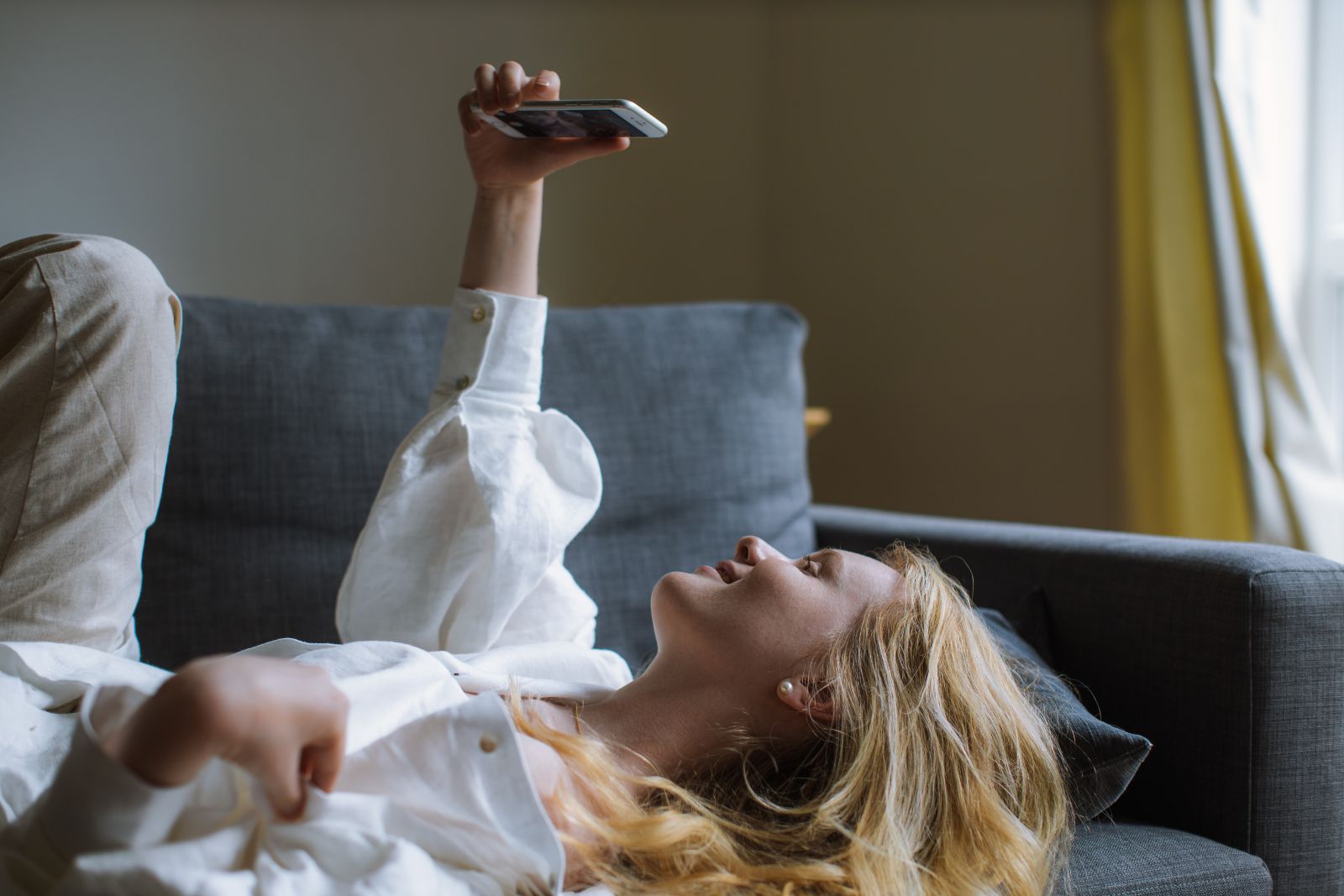 Mulher sozinha deitada no sofá tirando uma foto de si mesma com o celular
