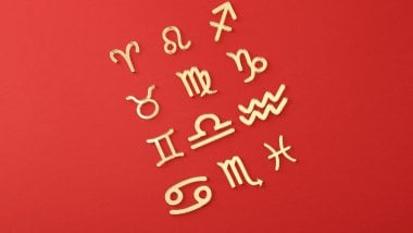 Os símbolos dos signos do zodíaco estão espalhados sobre uma superfície vermelha.