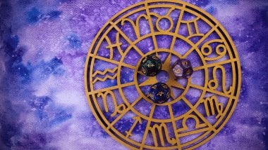 Há uma Roda do Zodíaco com os símbolos dos signos em volta. No meio, há alguns dados.