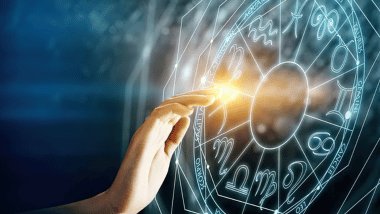 Mão tocando um círculo astrológico luminoso com símbolos do zodíaco, emitindo luz dourada em fundo azul.