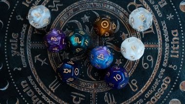 Imagem de uma mandala astrológica com 9 pedras de cristal coloridas e com os elementos dos signos desenhados sobre elas.