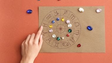 Imagem de fundo marrom avermelhado e em destaque uma mandala astrológica feita em papel cartão e sobre elas, pedras e cristais coloridos.