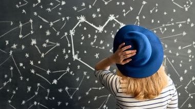 Imagem de aspectos astrológicos desenhados em um quadro negro e em destaque uma mulher olhando para este quadro negro, analisando as previsões.