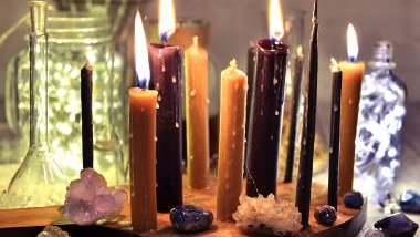 Imagem de uma mesa com várias velas acesas, pedras e cristais coloridos, simbolizando um ritual de amor e prosperidade para o ano novo.