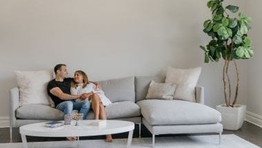 Imagem de um casal apaixonado, sentados em um sofá em uma sala de estar.