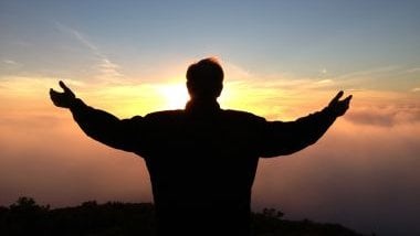 Imagem de silhueta masculina de braços aberto olhando para o pôr do sol, simbolizando a conexão com a espiritualidade.