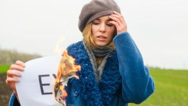 Imagem de uma mulher usando roupas de inverno e em uma das mãos ela segura um cartaz com a palavra EX, sendo queimado.