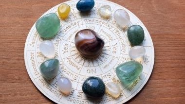 Imagem de uma mandala astrológica na cor branca sobre uma mesa de madeira. Sobre a mandala, cristais em cada um dos signos.