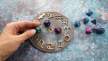 Imagem de uma mão feminina colocando um cristal de cor verde, com os glifos dos signos desenhados sobre uma mandala astrológica.