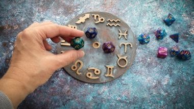 Imagem de uma mão feminina manipulando pedras de cristais coloridas sobre uma mandala astrológica com os elementos dos 12 signos.