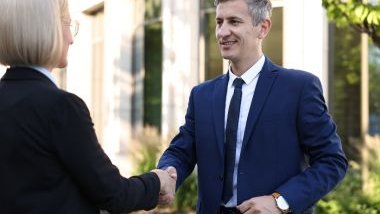 Imagem de um homem cumprimento uma mulher, ambos usam terno e simbolizam uma pessoa que tem diplomacia.