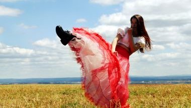 Imagem de uma cabocla no campo. Ela usa vestido branco com uma saia de tule vermelha. A foto traz o conceito da cabocla Iara da Umbanda.