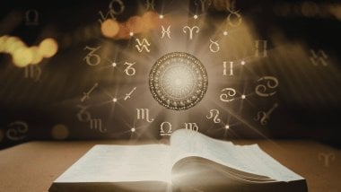 Livro aberto com círculo astrológico luminoso e símbolos do zodíaco flutuando acima, em tons dourados.