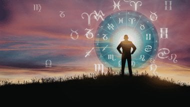 Silhueta de pessoa em pé ao pôr do sol com um círculo astrológico luminoso e símbolos do zodíaco ao redor.