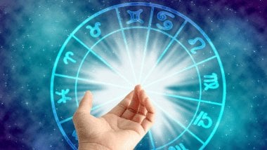 No foco da imagem, há uma Roda do Zodíaco e, na frente dela, há uma mão esticada de uma pessoa.