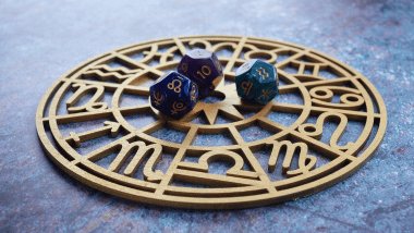 No foco da imagem, há uma Roda do Zodíaco com os símbolos dos signos e há dados em cima dela.