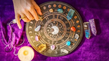 No foco da imagem, há uma Roda do Zodíaco com os símbolos dos signos e há cristais em cima dela.