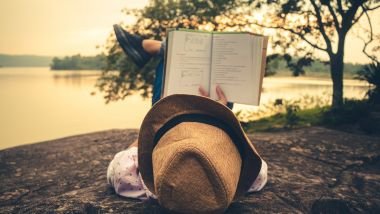 Imagem de uma mulher deitada sobre uma pedra em frente a um lago, lendo um livro, curtindo o seu momento de silêncio e paz.