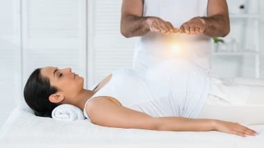 Imagem de um reikiano aplicando a técnica do reiki em uma mulher deitada sobre uma maca.