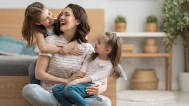 Imagem de uma mãe sentada no chão da sala, brincando com as suas duas filhas menores. A foto simboliza o dia das mães e como é a mãe de cada signo.