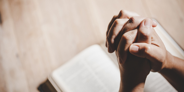 Pessoa orando com a bíblia no colo