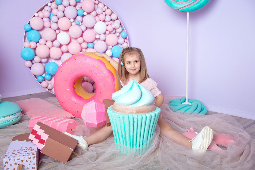 Criança sentada atrás de cupcake gigante e doces