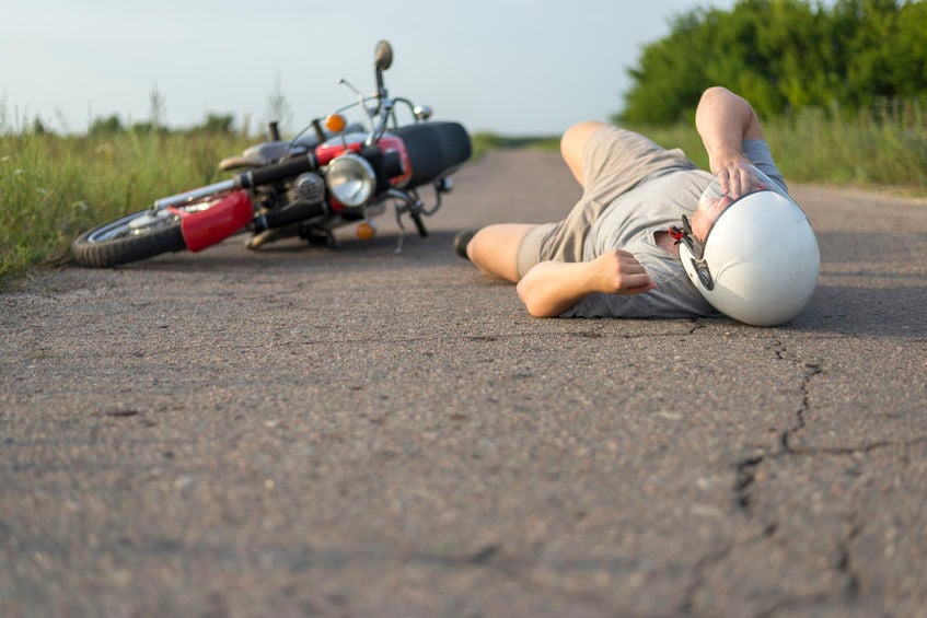 Homem caído em asfalto após acidente de moto