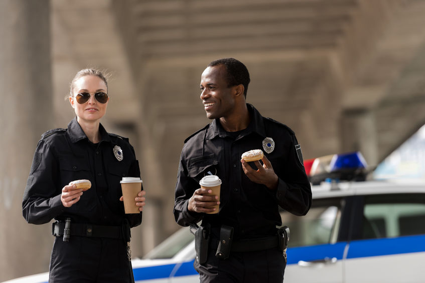 Dois policiais com café e donuts em frente à viatura