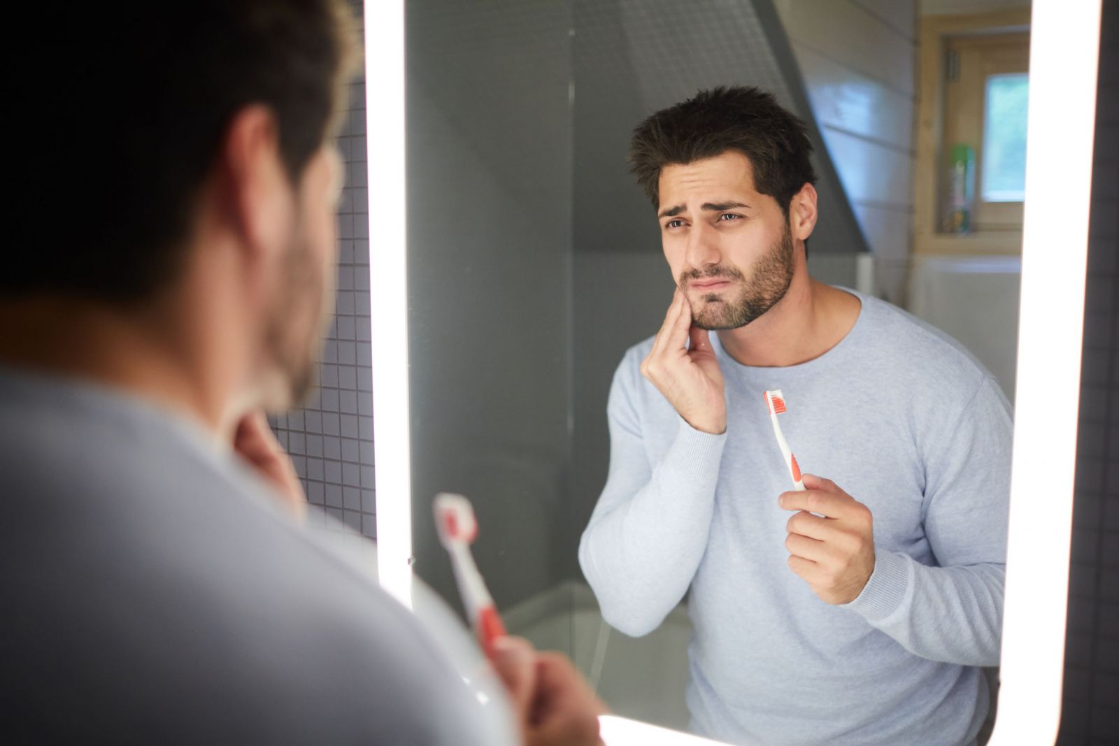 Homem sentindo dor de dente e segurando escova de dente
