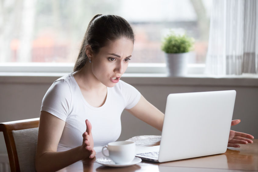 Mulher branca em frente ao computador com expressão brava.