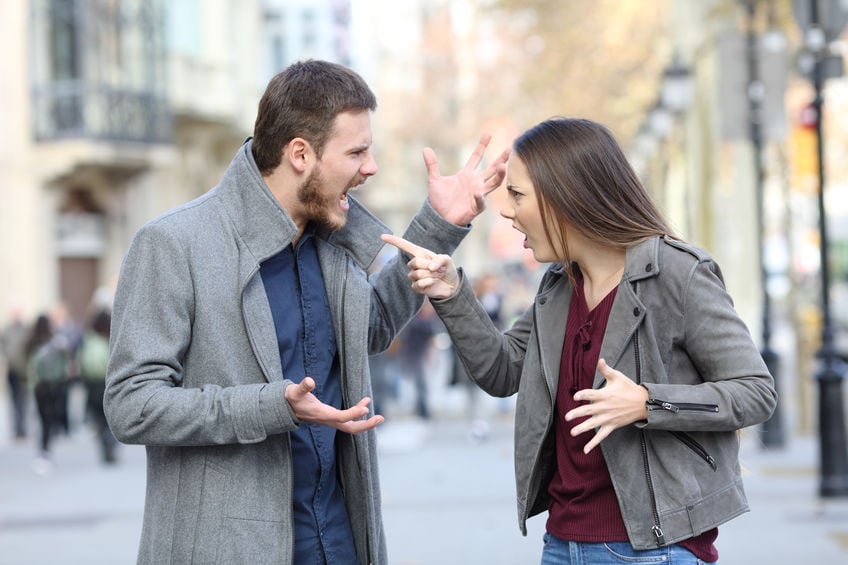 Homem e mulher brancos discutindo na rua.