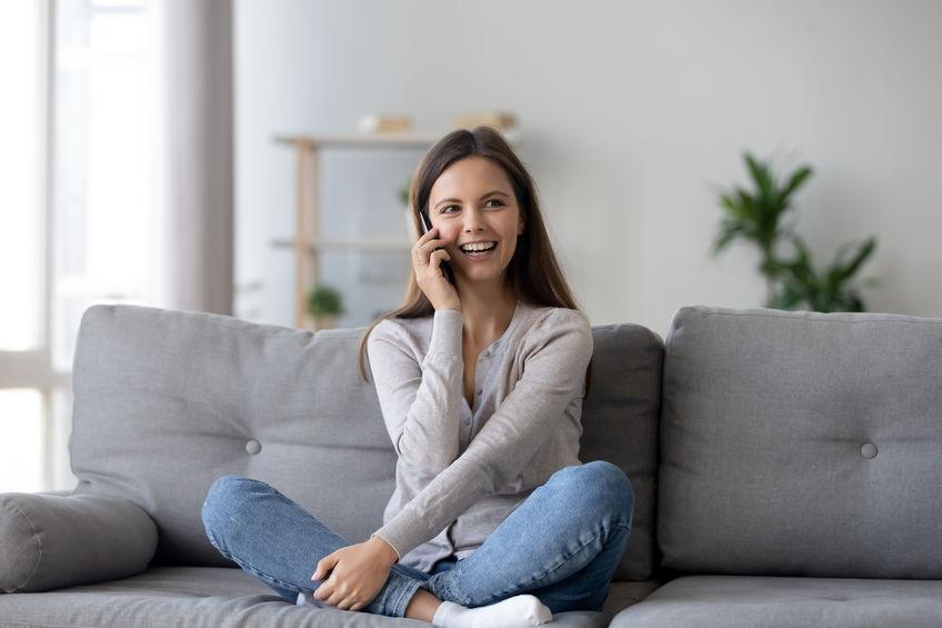 Mulher tranquila e sentada no sofá falando no celular