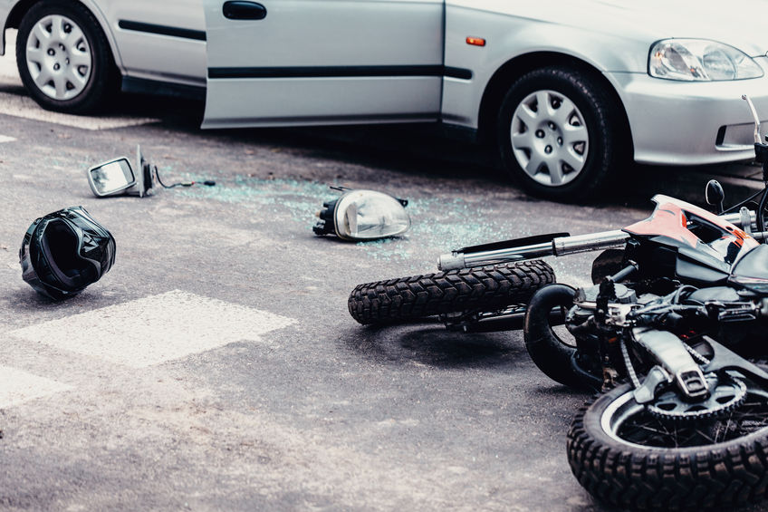 Moto e capacete jogados no chão e carro ao lado