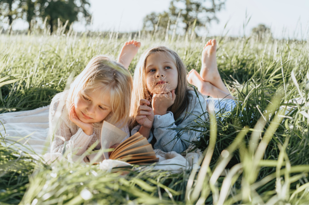 duas meninas deitadas na grama lendo livro e pensando.