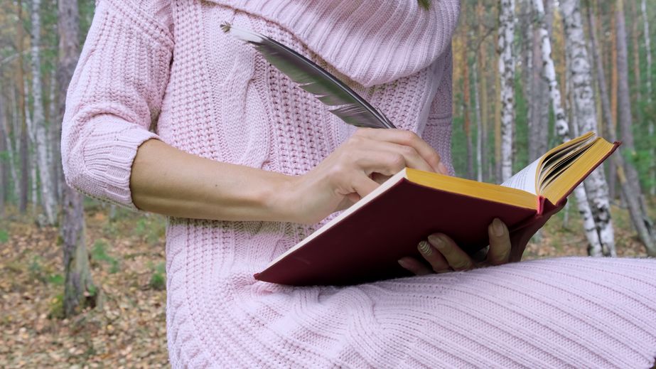 Pessoa escrevendo em um livro com uma pena no meio de uma floresta