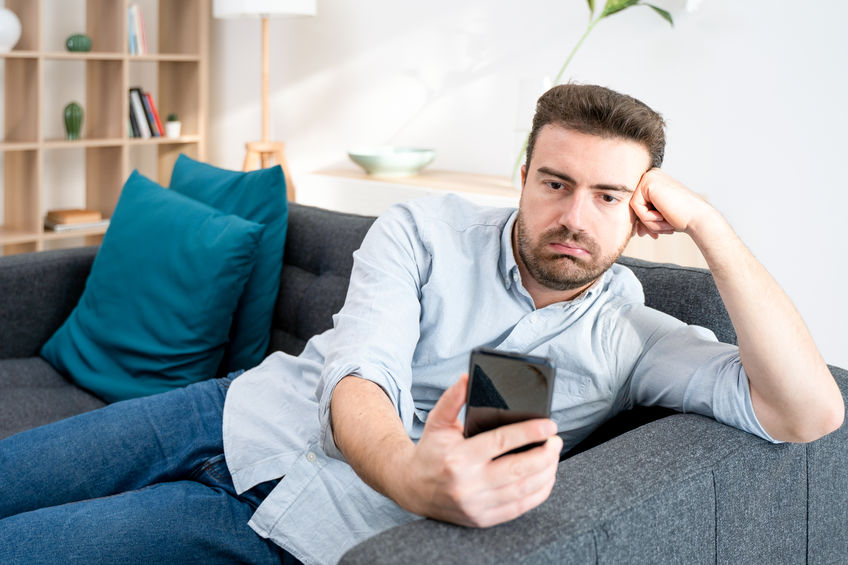 Homem sentado em sofá e olhando para celular