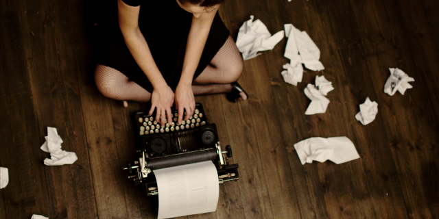 Escritora sentada no chão escrevendo em máquina de datilografia