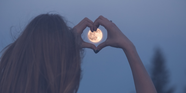Mulher fazendo um coração com as mãos para a lua cheia