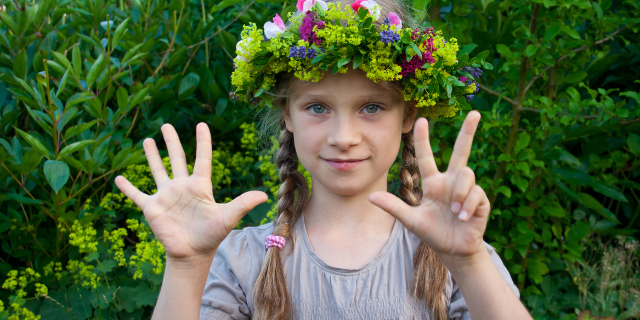 Criança com coroa de flores fazendo o número 8 com as mãos