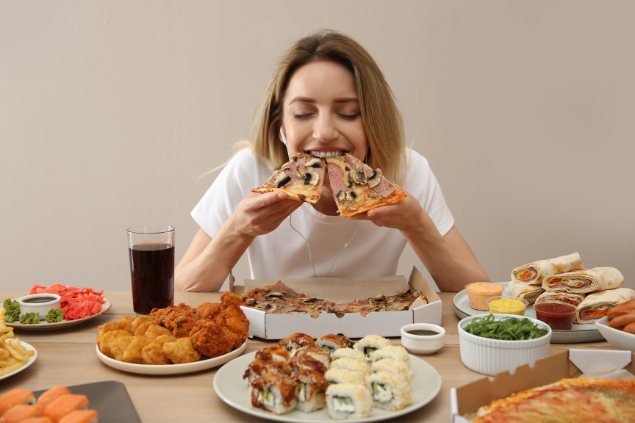 Mulher comendo dois pedaços de pizza enquanto a mesa está cheia de outras comidas.