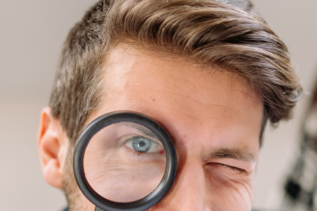 Homem de olho azul segurando uma lupa no olho