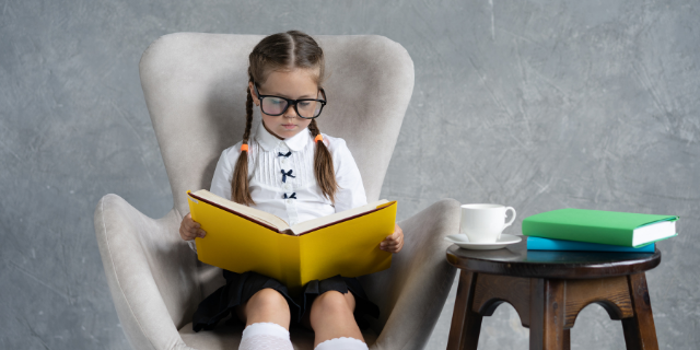 Menina sentada em uma poltrona enquanto lê um livro