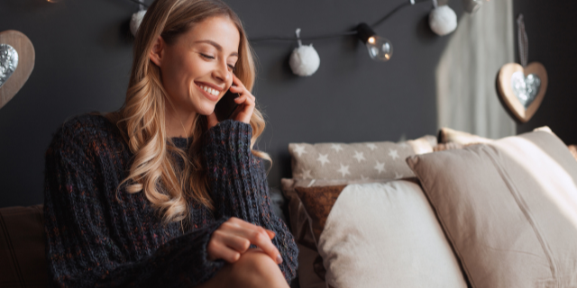 Mulher sorridente sentada no sofá enquanto conversa no telefone