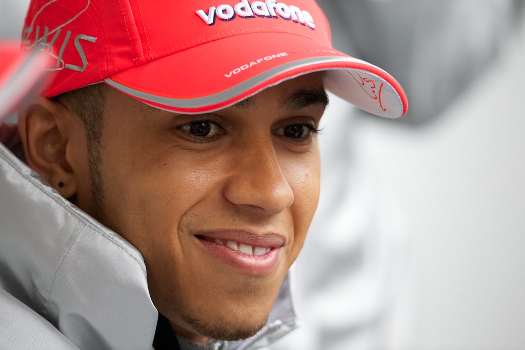Lewis Hamilton sorrindo usando boné e casaco de frio