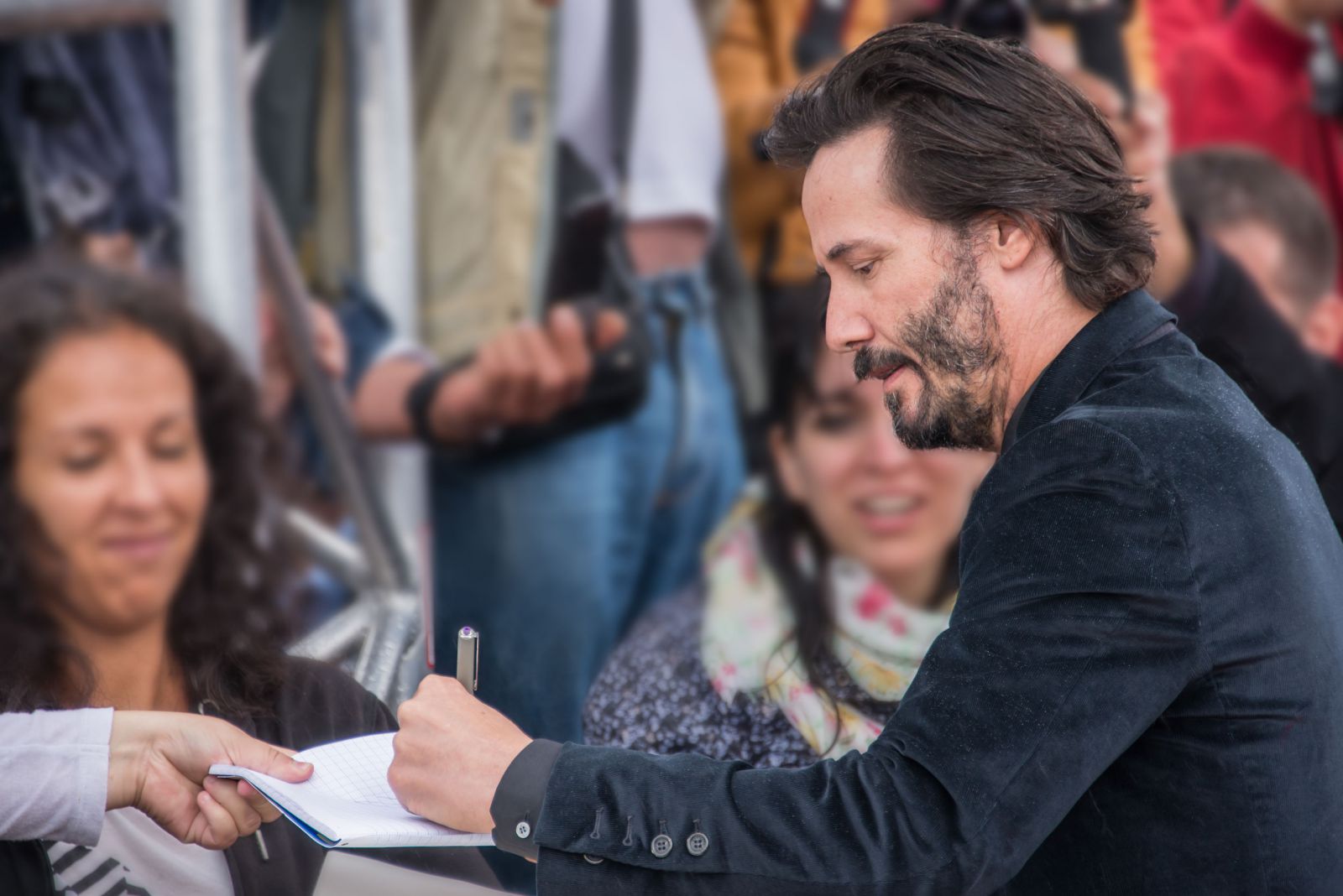 Keanu Reeves autografando caderno ao lado de fãs 