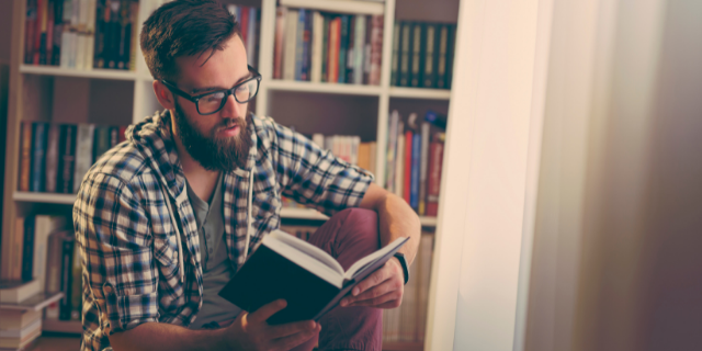 Homem de óculos lendo livro na biblioteca de casa