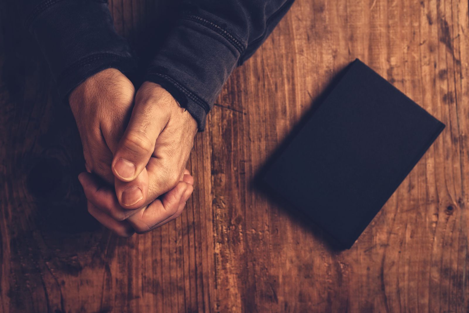 Mãos brancas rezando ao lado de uma bíblia.