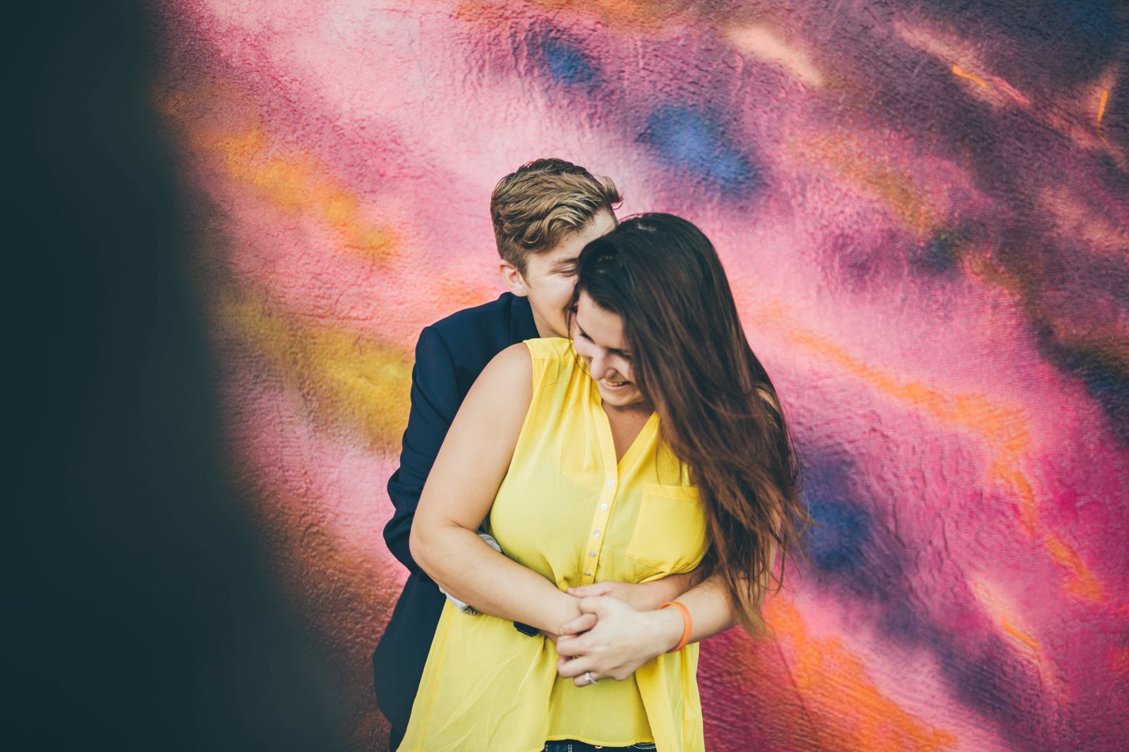 Casal se abraçando em frente a um muro colorido