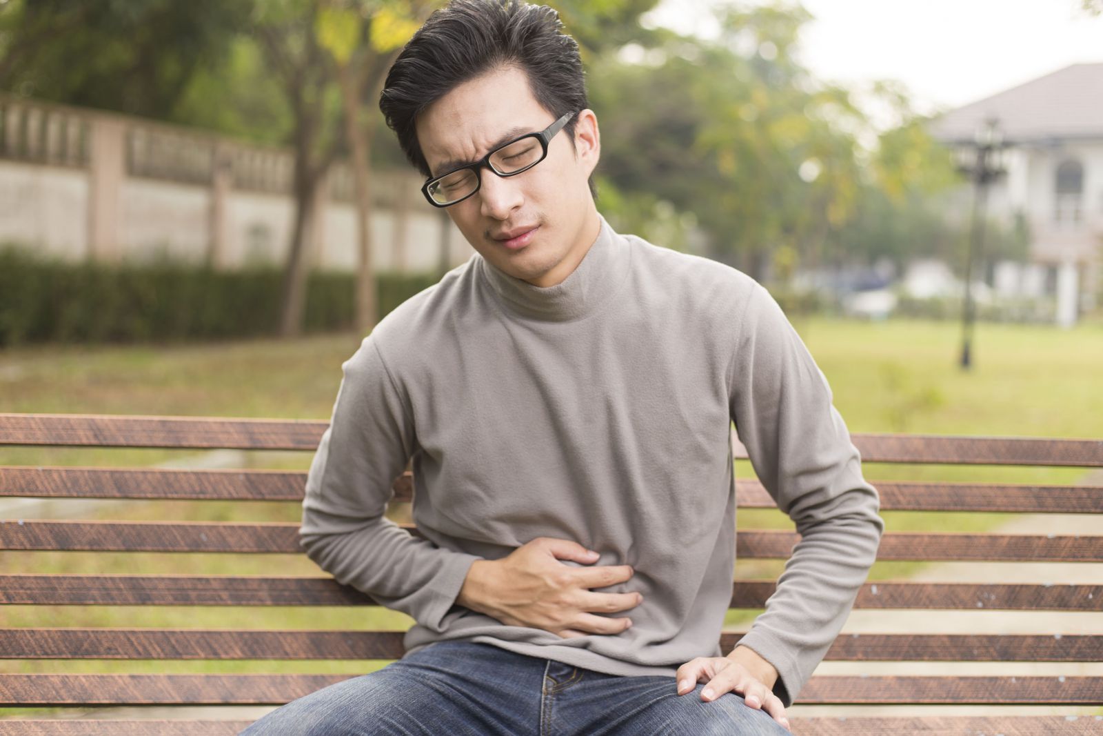 Homem sentado em um banco de praça com dor no estomago